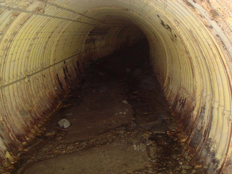 The tunnel beyond the fuel terminal: tons of dirt and rock have washed in and covered the floor.  The water cuts small tributaries through the dirt as it passes.